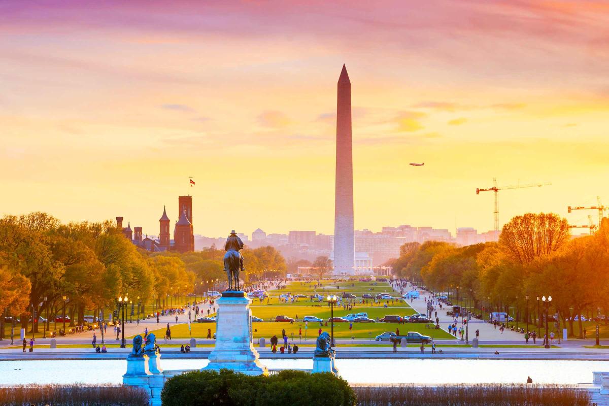 Đài tưởng niệm Washington vào mùa thu lúc hoàng hôn với hàng cây lá vàng cam và bầu trời rực sắc hồng vàng.