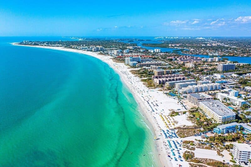 Hình ảnh từ trên cao cho thấy một bãi biển rực rỡ với làn nước màu ngọc lam ở Siesta Key, Florida. Dọc theo bờ biển là khung cảnh trải dài với những người tắm nắng và những chiếc ô che nắng.