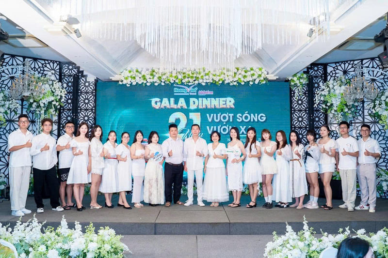 Tập thể văn phòng 28 Hoàng Việt Travel mặc đồ trắng giơ ngón tay cái chụp ảnh trên sân khấu Gala Dinner 21 năm