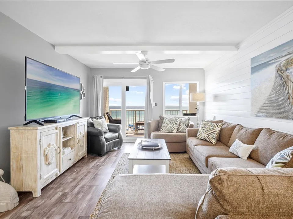 Phòng khách ven biển với bộ sofa nâu, kệ TV gỗ và cửa kính lớn dẫn ra ban công hướng biển