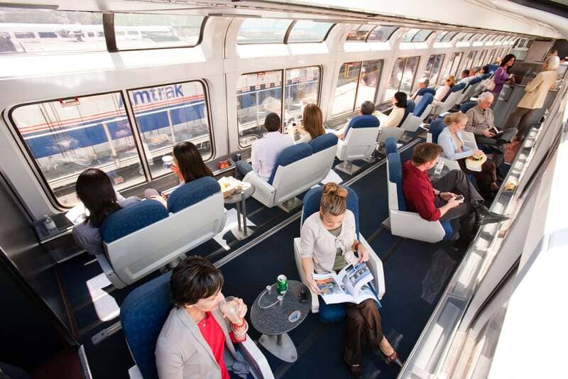 Hành khách ngồi thư giãn bên cửa kính panorama lớn bên trong toa ngắm cảnh tàu Amtrak