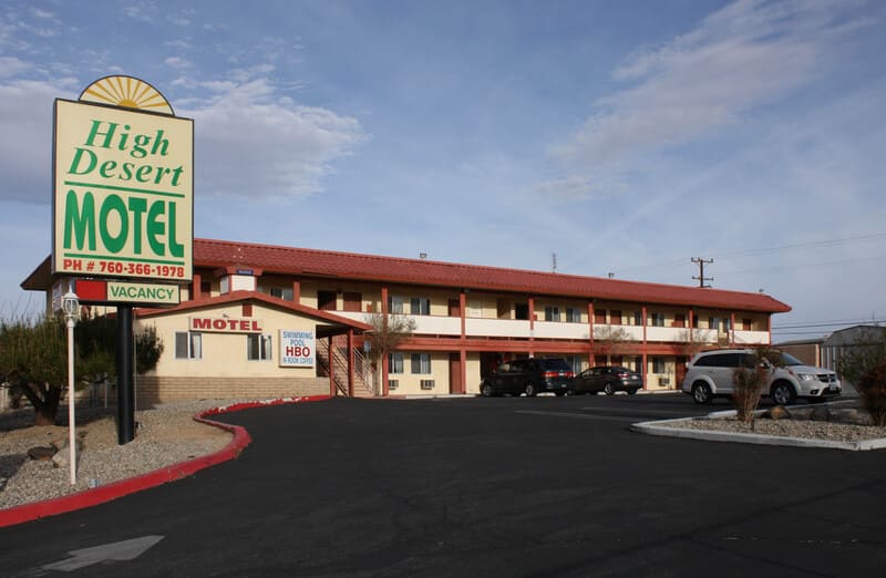 Tòa nhà High Desert Motel 2 tầng mái đỏ với biển hiệu lớn và bãi đỗ xe phía trước