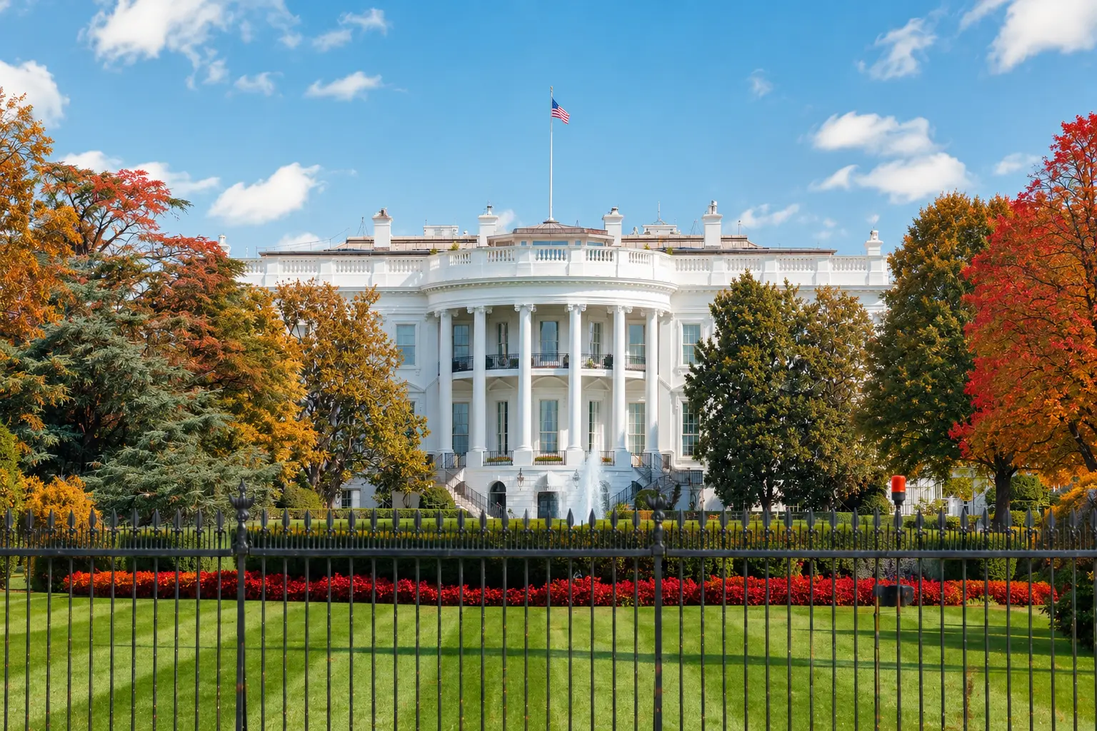 Nhà Trắng ở Washington, D.C. vào mùa thu với kiến trúc màu trắng, quốc kỳ Mỹ và hàng cây lá đỏ vàng bao quanh.