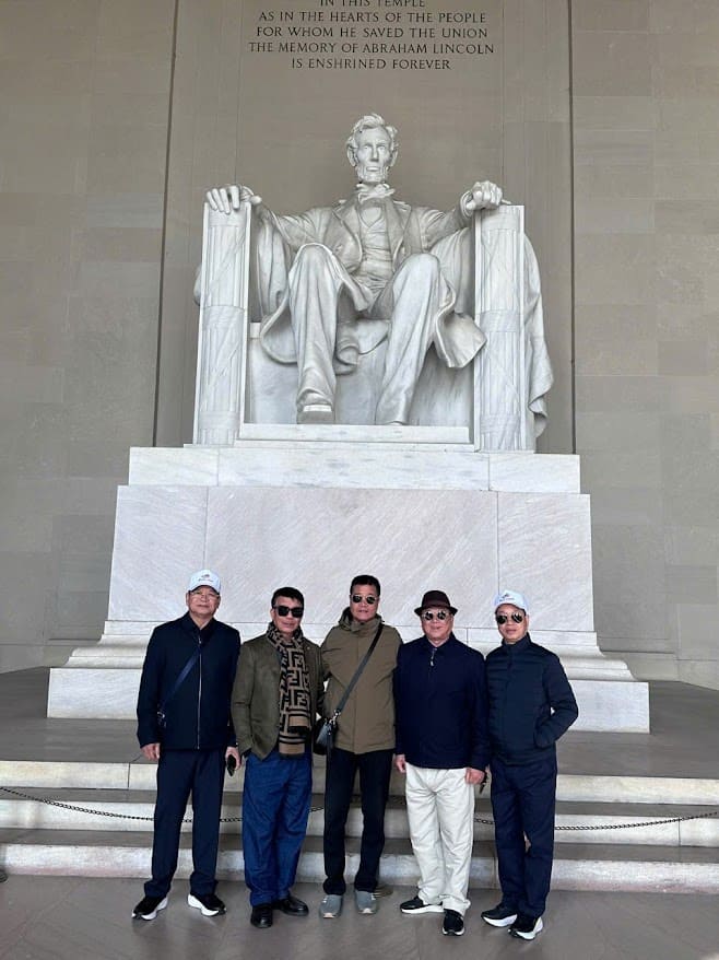 Năm người đứng mỉm cười trước bức tượng lớn của Abraham Lincoln tại Đài tưởng niệm Lincoln. Khung cảnh trang trọng và đầy vẻ tôn kính.