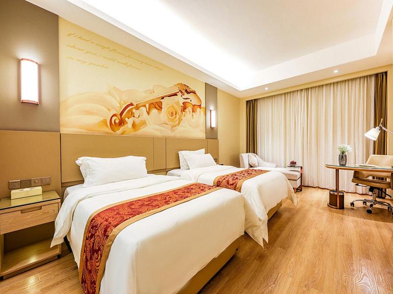 Phòng khách sạn hai giường đơn phủ ga trắng, mảng tường đầu giường vẽ đàn violin, sàn gỗ và bàn làm việc