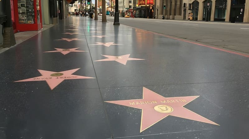 Những ngôi sao trên Đại lộ Danh vọng Hollywood trải dài trên vỉa hè sáng bóng, mang theo những cái tên như Marion Martin. Khung cảnh yên bình, với những tòa nhà nằm dọc theo con phố vắng vẻ.