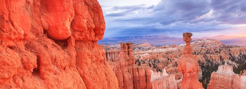 Khung cảnh hùng vĩ của Bryce Canyon lúc hoàng hôn, với những khối đá đỏ rực rỡ và các cột đá hình nấm, cùng bầu trời nhiều mây càng làm tăng thêm vẻ tráng lệ của khung cảnh.