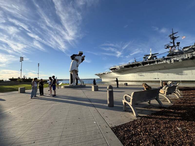 Tượng thủy thủ hôn y tá và tàu sân bay USS Midway tại công viên San Diego, xung quanh có vài du khách