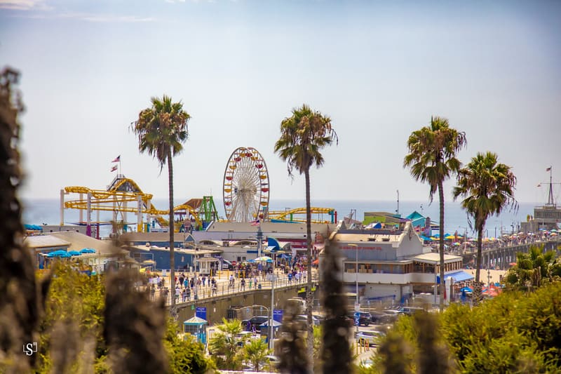 Khu vui chơi trên bến tàu Santa Monica với vòng đu quay lớn, tàu lượn siêu tốc màu vàng và hàng cọ vươn cao trước biển