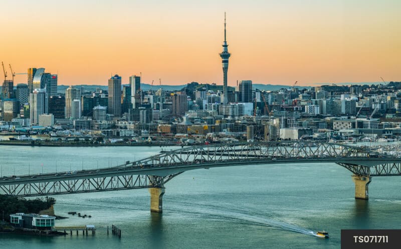 Cầu Auckland Harbour Bridge trên biển và tháp Sky Tower nổi bật giữa toàn cảnh thành phố lúc hoàng hôn