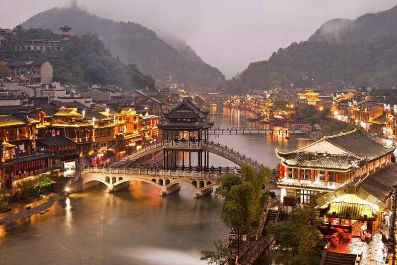 Phượng Hoàng cổ trấn với cầu Hồng bắc qua sông Đà Giang, dãy nhà cổ hai bên lên đèn vàng và núi mờ sương phía xa