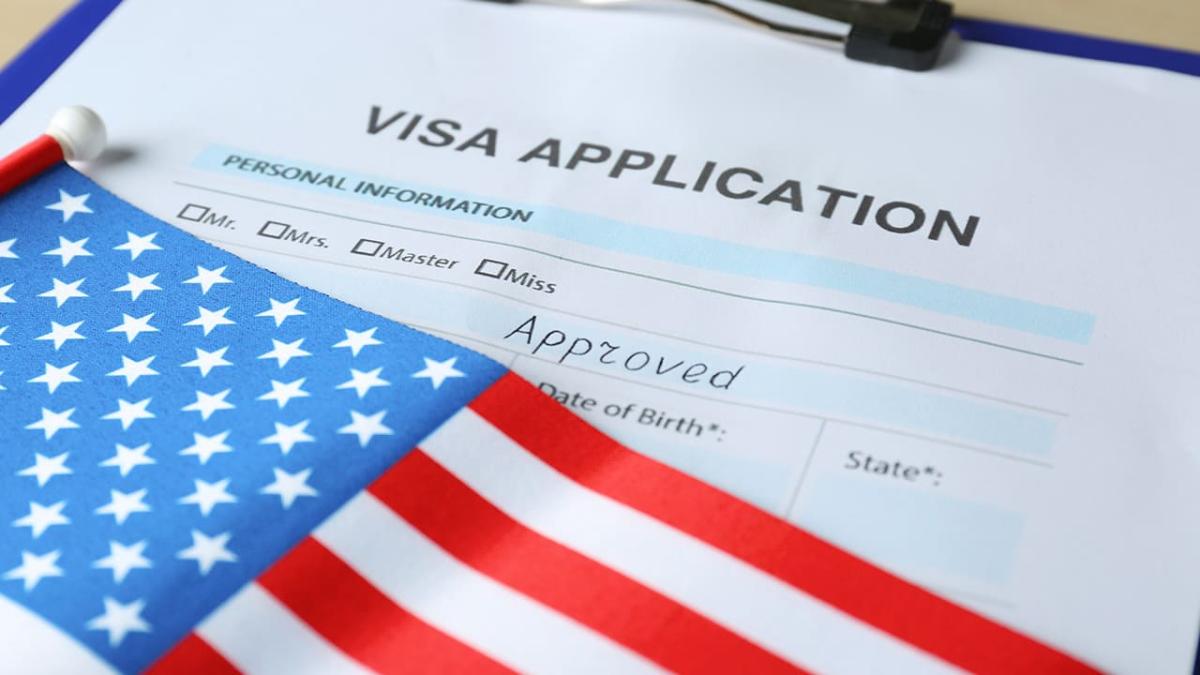 Mẫu đơn xin visa có ghi chữ "Đã duyệt". Một lá cờ Mỹ được phủ lên góc của mẫu đơn, tượng trưng cho sự thành công và lòng yêu nước.