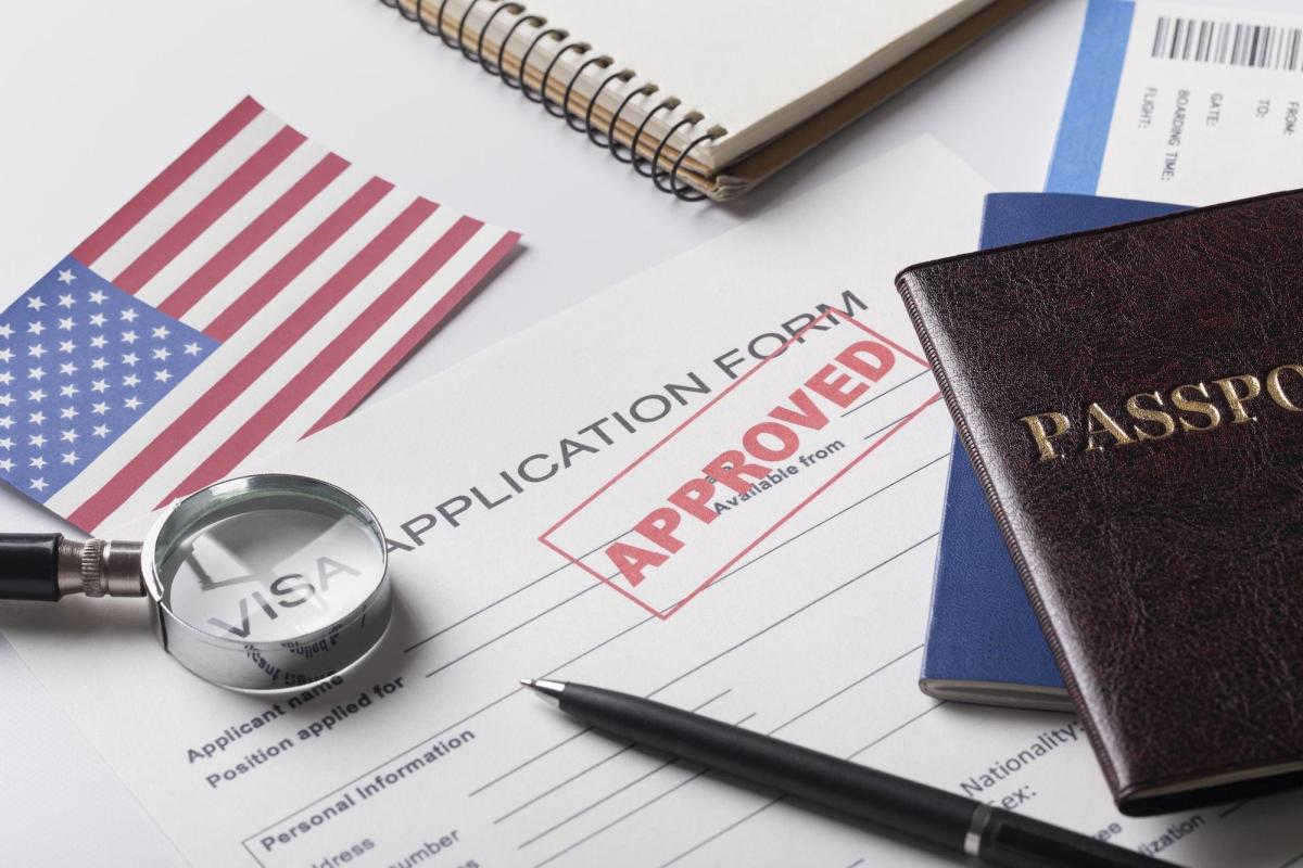 Mẫu đơn xin visa có đóng dấu "Đã duyệt" màu đỏ, cờ Mỹ, hộ chiếu, kính lúp và bút trên bàn, thể hiện sự chấp thuận thành công.