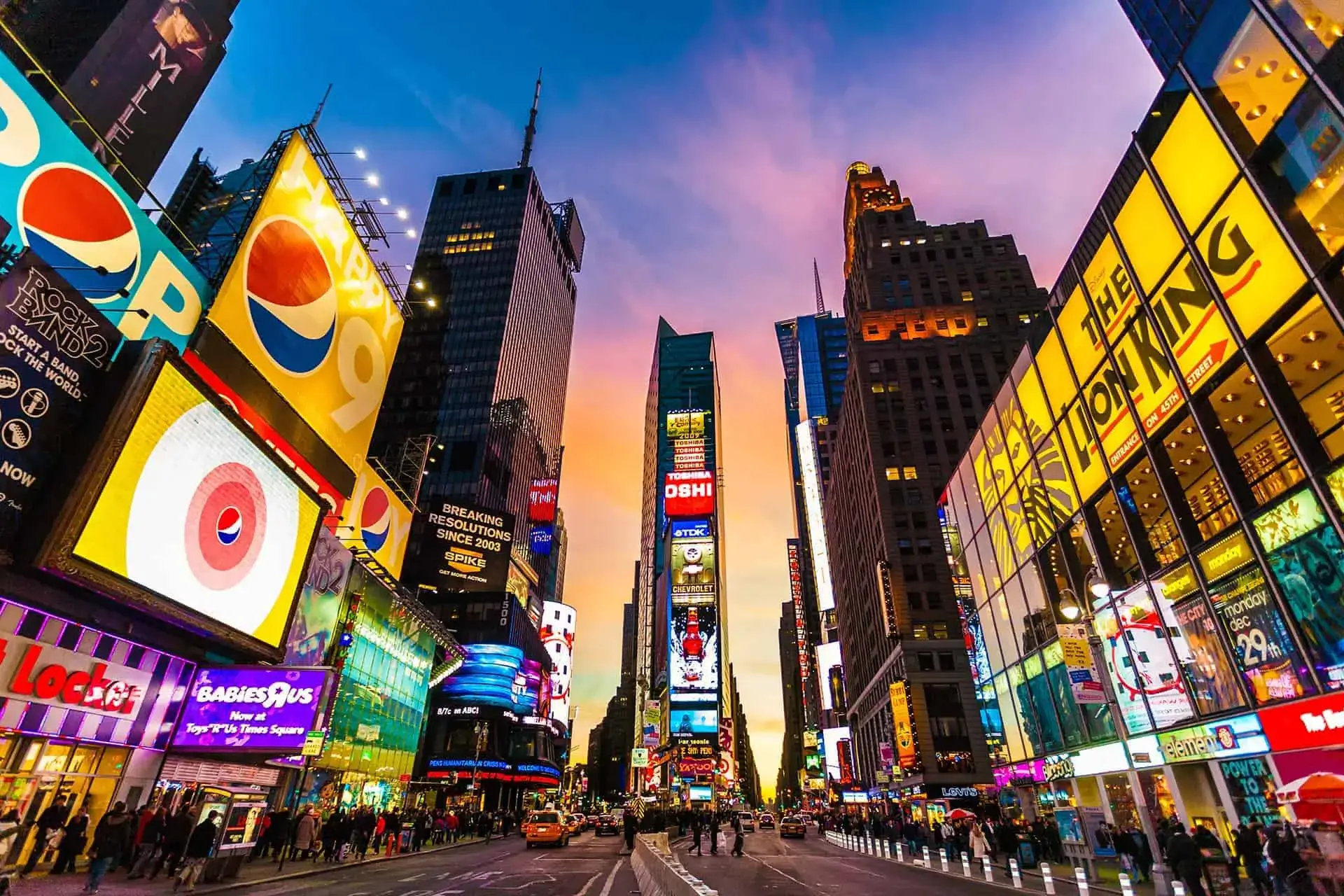 Quảng trường Times Square lúc hoàng hôn, những bảng quảng cáo rực rỡ và màn hình kỹ thuật số thắp sáng con phố nhộn nhịp, dưới bầu trời hoàng hôn ngoạn mục, tạo nên một khung cảnh đô thị đầy năng động.