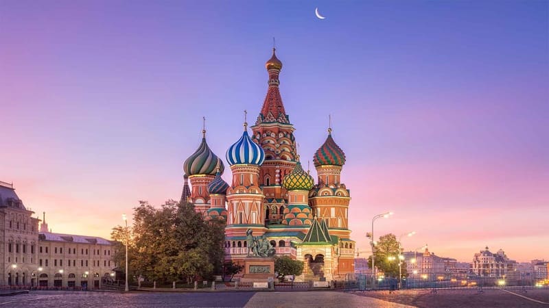 Nhà thờ Thánh Basil ở Moscow lúc hoàng hôn, với những mái vòm hình củ hành đầy màu sắc dưới ánh trăng lưỡi liềm trên nền trời hồng tím, tạo nên một khung cảnh thanh bình và đẹp như tranh vẽ.