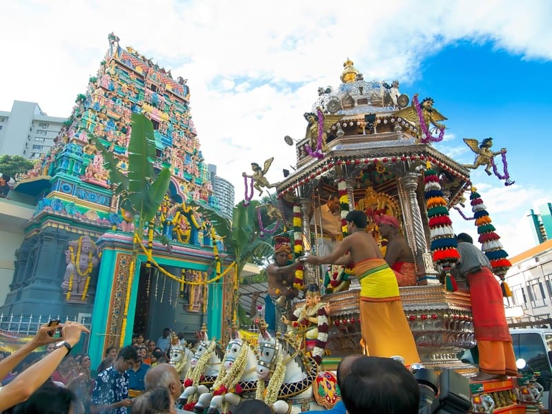 Lễ hội đền thờ Hindu đầy màu sắc với cỗ xe được trang trí công phu, điểm xuyết bằng hoa và tượng. Các tín đồ trong trang phục rực rỡ tham gia các nghi lễ dưới bầu trời trong xanh.