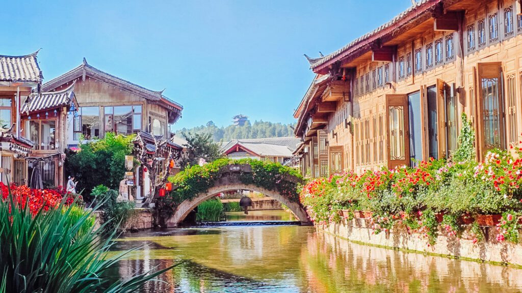 Kiến trúc truyền thống Trung Hoa nằm dọc theo một con kênh yên tĩnh, được tô điểm bởi những bông hoa và cây xanh rực rỡ. Một cây cầu đá uốn cong duyên dáng ở giữa.