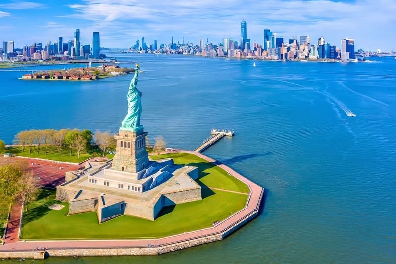 Ảnh chụp từ trên cao tượng Nữ thần Tự do trên đảo Liberty, bao quanh là nước. Xa xa là đường chân trời Manhattan dưới bầu trời xanh trong. Thật hùng vĩ và mang tính biểu tượng.