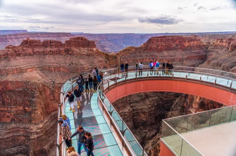 Du khách đi bộ trên cầu Skywalk Grand Canyon, một cây cầu kính bắc ngang qua một hẻm núi sâu. Từ đây có thể nhìn thấy toàn cảnh hẻm núi rộng lớn và những khối đá đỏ hùng vĩ.