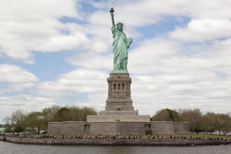 Tượng Nữ thần Tự do sừng sững dưới bầu trời nhiều mây trên đảo Liberty. Du khách có thể được nhìn thấy ở chân tượng, thể hiện sự ngưỡng mộ.