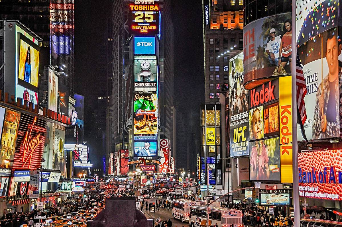 Quảng trường Times Square rực rỡ về đêm, nhộn nhịp với người đi bộ và xe cộ. Những biển quảng cáo và biển hiệu đèn neon rực rỡ tạo nên một bầu không khí sống động và tràn đầy năng lượng.