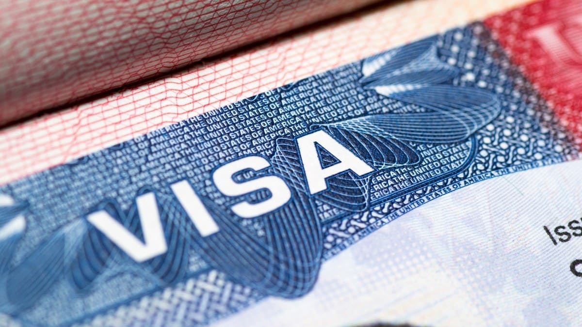 Ảnh cận cảnh thị thực Hoa Kỳ với chữ "VISA" được in đậm màu trắng nổi bật trên nền xanh có họa tiết, tạo cảm giác đây là một tài liệu chính thức.