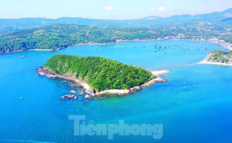 Ảnh chụp từ trên cao cho thấy một hòn đảo xanh tươi tốt được bao quanh bởi làn nước trong xanh, với những ngọn đồi xa xa và những chiếc thuyền rải rác ở phía sau.