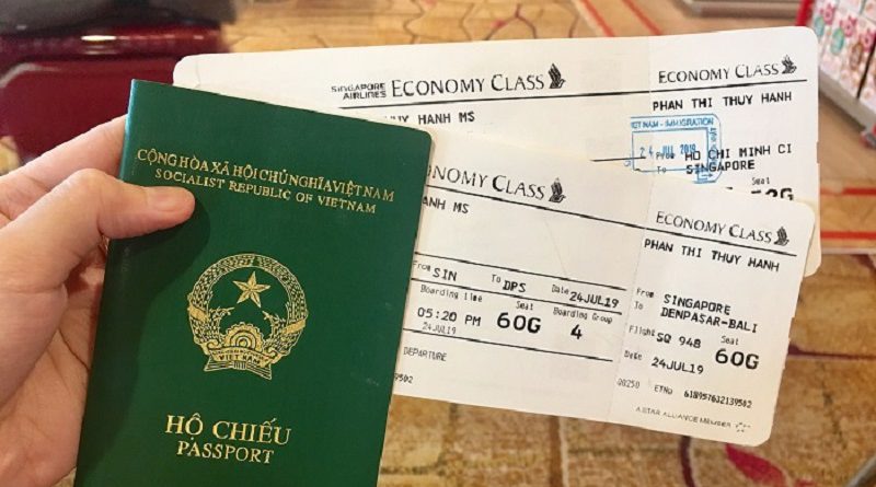 Một bàn tay cầm hộ chiếu Việt Nam màu xanh lá cây và hai thẻ lên máy bay hạng phổ thông của hãng Singapore Airlines. Bối cảnh gợi lên môi trường sân bay.