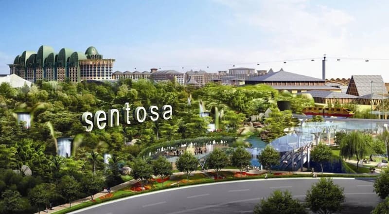 Những tán cây xanh mướt và thác nước bao quanh sườn đồi với dòng chữ "Sentosa" màu trắng nổi bật. Những tòa nhà hiện đại và tuyến cáp treo hiện ra ở phía xa.