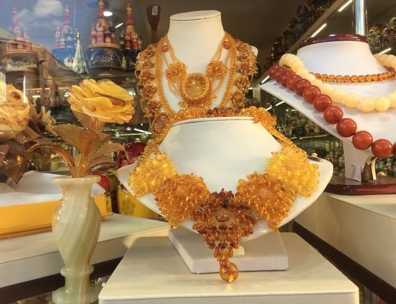 Những món trang sức hổ phách sang trọng được trưng bày trên ba bức tượng bán thân, với những chiếc vòng cổ và vòng tay được chế tác tinh xảo. Một bông hồng vàng trong bình càng làm tăng thêm vẻ sang trọng, cùng với những hình ảnh phản chiếu của các họa tiết trang trí cầu kỳ trên mặt kính, càng làm nổi bật vẻ thanh lịch của khung cảnh.