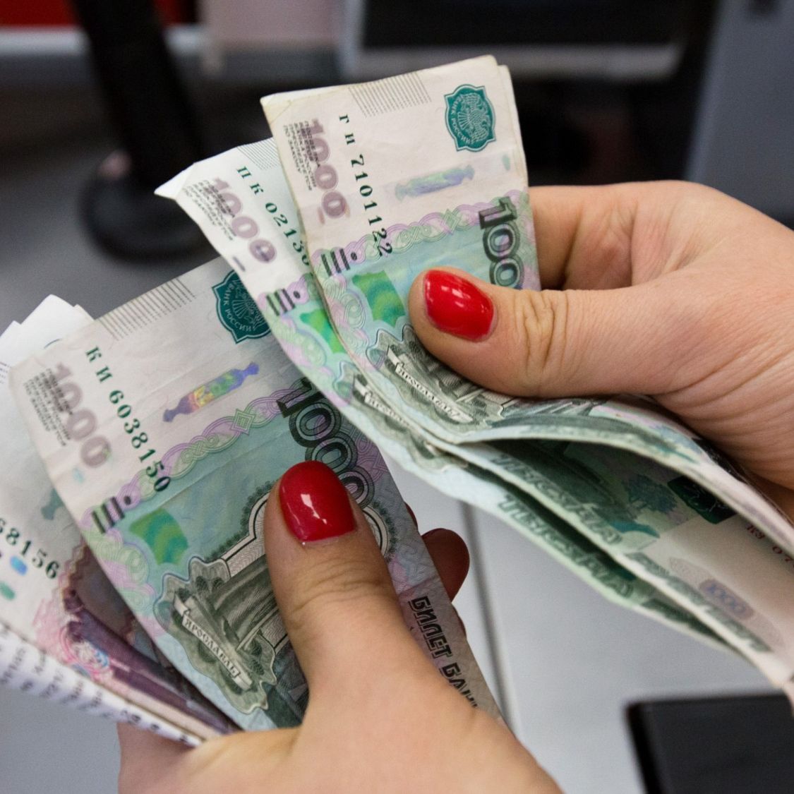 Đôi bàn tay với móng tay sơn đỏ đang cầm và đếm vài tờ tiền mệnh giá 100 rúp Nga. Cảnh tượng này gợi ý việc xử lý tiền bạc, có thể trong bối cảnh tài chính.