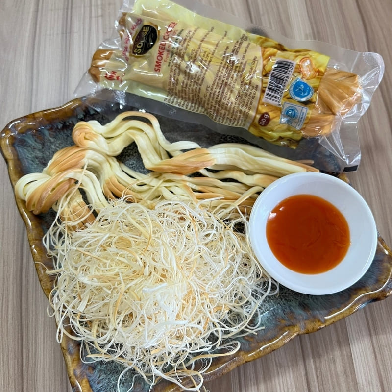 Một chiếc khay sứ đựng phô mai hun khói xoắn và phô mai bào sợi bên cạnh một bát nhỏ nước sốt cà chua. Một khối phô mai đóng gói nằm ở phía sau.