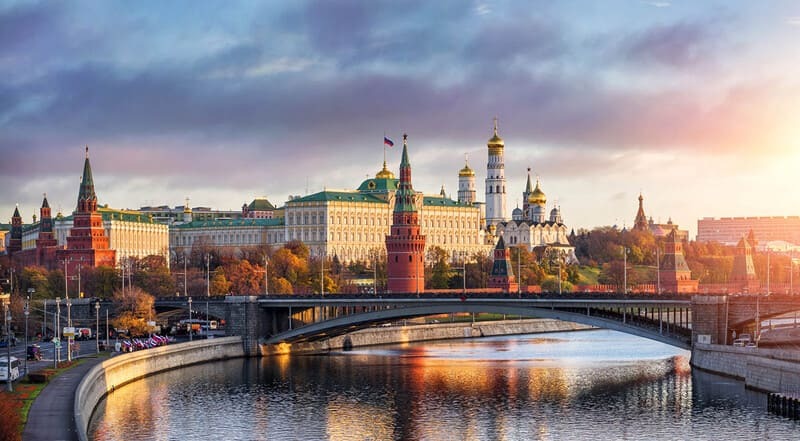 Cảnh quan tuyệt đẹp của Điện Kremlin ở Moscow lúc hoàng hôn, với những tòa tháp biểu tượng và mái vòm vàng rực. Dòng sông Moskva phản chiếu bầu trời ấm áp, rực rỡ.