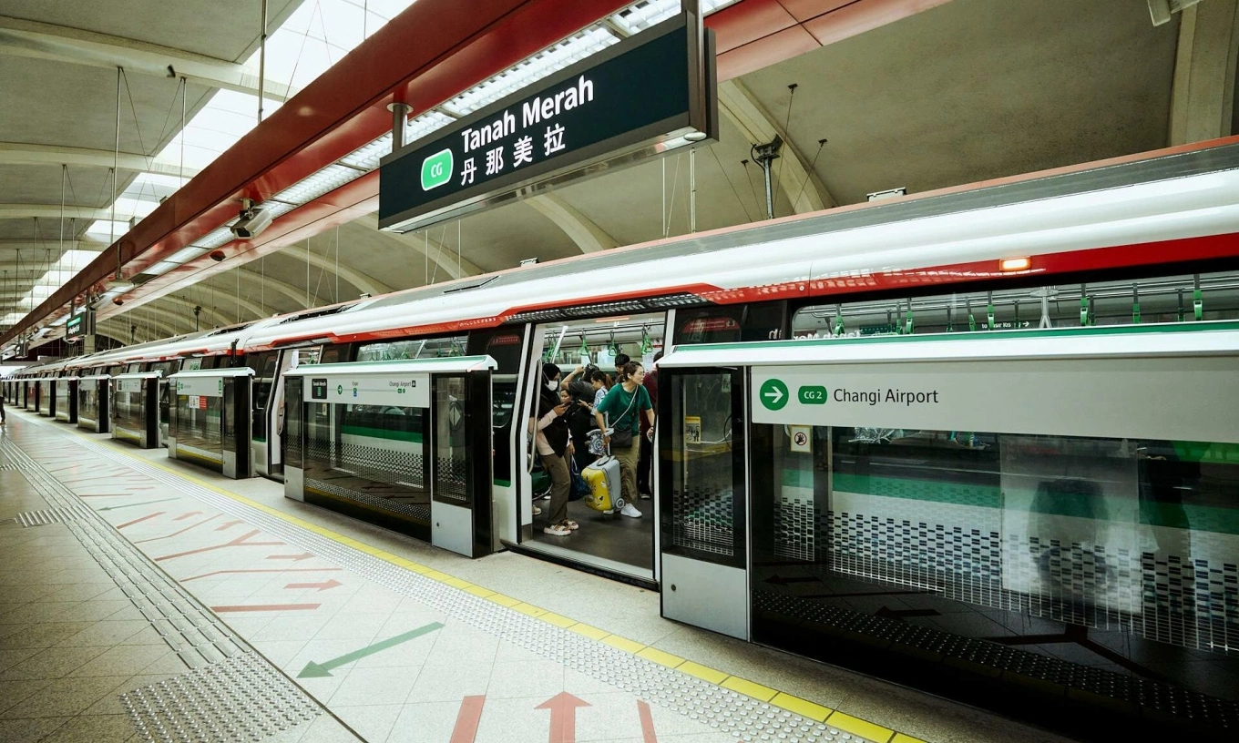 Một chuyến tàu đến ga Tanah Merah ở Singapore. Hành khách lên và xuống tàu. Sân ga sạch sẽ, có biển chỉ dẫn mũi tên và biển báo nhà ga rõ ràng.