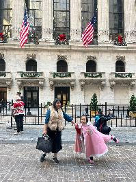 Một khung cảnh vui tươi bên ngoài một tòa nhà lịch sử với những lá cờ Mỹ. Một người phụ nữ và hai đứa trẻ mặc đồ màu hồng đang nô đùa, thể hiện niềm hạnh phúc và sự gắn kết.