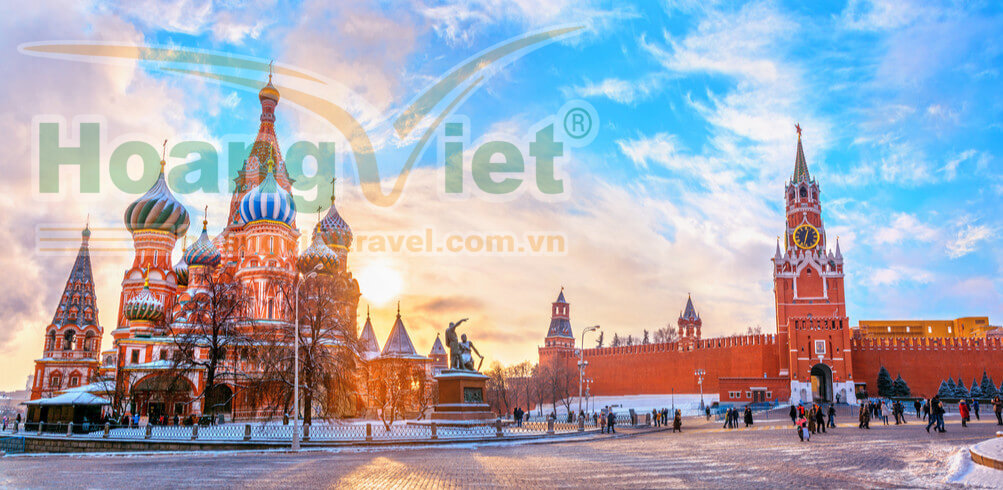 Quảng trường Đỏ ở Moscow lúc hoàng hôn, với Nhà thờ Thánh Basil có những mái vòm hình củ hành đầy màu sắc ở bên trái và Tháp Spasskaya ở bên phải, cùng nhiều người đang đi dạo.