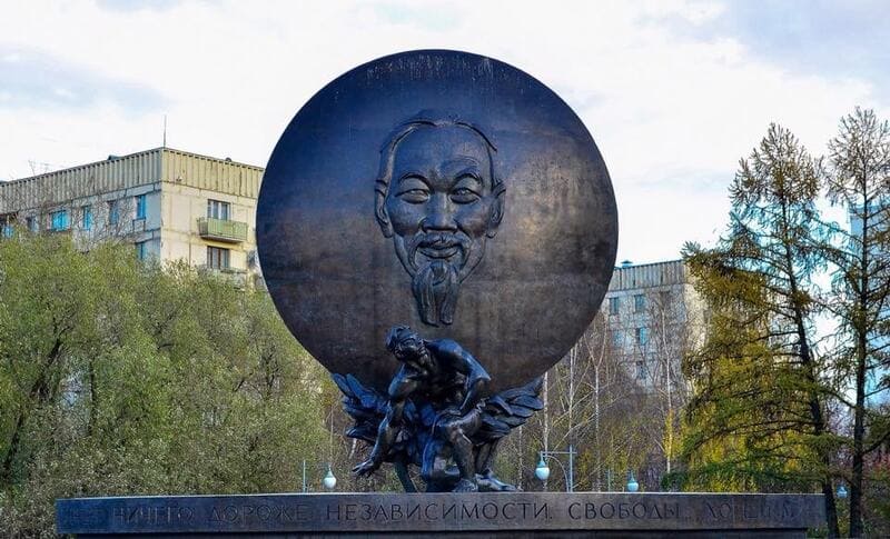 Một tác phẩm điêu khắc phù điêu bằng đồng, mô tả một vòng tròn lớn với khuôn mặt có râu phía trên một hình người ngồi trên bệ. Cây cối và các tòa nhà nằm ở phía sau.