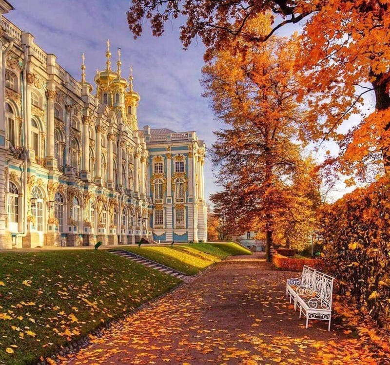 Cung điện mùa thu với những chi tiết màu xanh lam và vàng nằm cạnh con đường rợp bóng cây phủ đầy lá mùa thu. Một chiếc ghế dài màu trắng có thể nhìn thấy ở bên phải.
