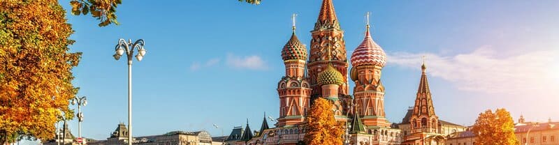 Nhà thờ St. Basil với những mái vòm hình củ hành đầy màu sắc được bao quanh bởi những tán cây mùa thu dưới bầu trời xanh trong vắt, tạo nên một khung cảnh sống động và đậm chất lịch sử.